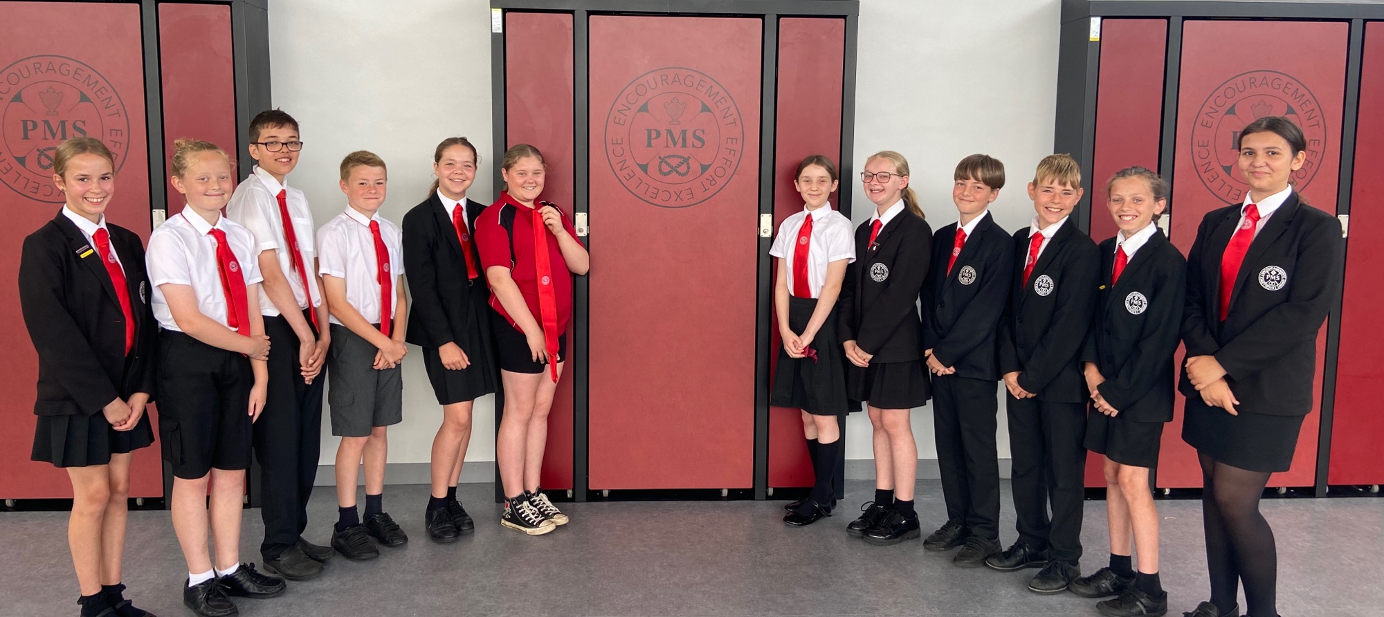 A group of Penkridge Middle School students wearing official uniforms, standing in front of a red and grey background.  